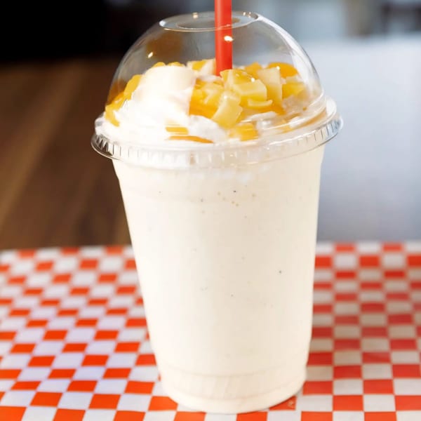 A SMA5H milkshake with whipped cream and diced mango, served in a clear cup with a red straw.