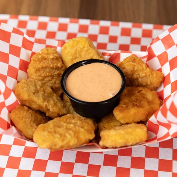 Golden-brown chicken nuggets and a cup of dipping sauce in a red and white checkered paper tray.