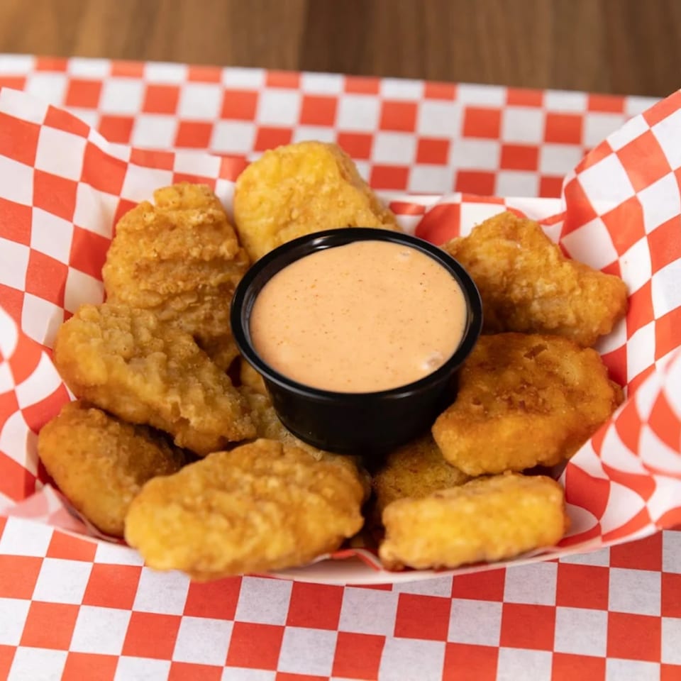 Golden-brown SMA5H chicken nuggets and dipping sauce in a red and white checkered paper tray.