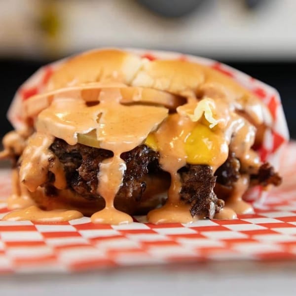 A SMA5H burger with melted cheese, pickles, onions, and special sauce on a red and white checkered wrapper.