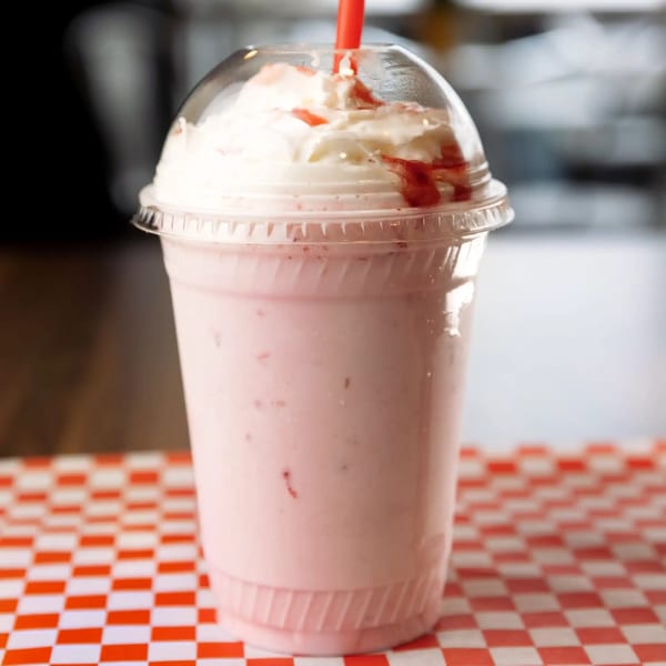 A SMA5H strawberry milkshake with whipped cream and a red straw on a red and white checkered paper.