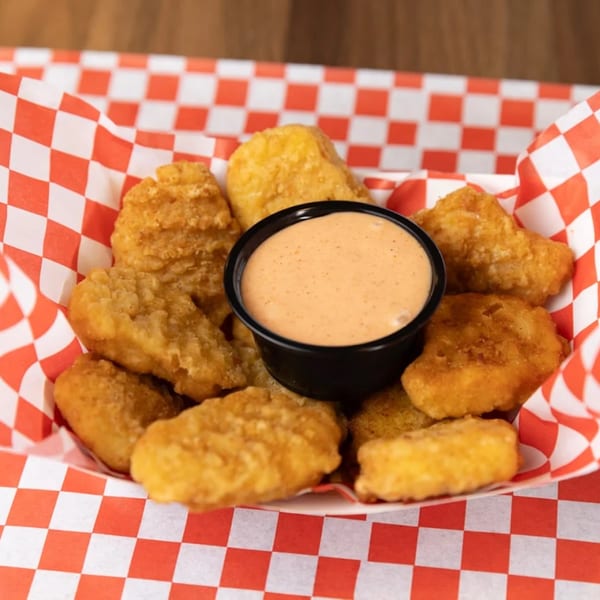 Golden-brown chicken nuggets with a side of dipping sauce in a red and white checkered basket.