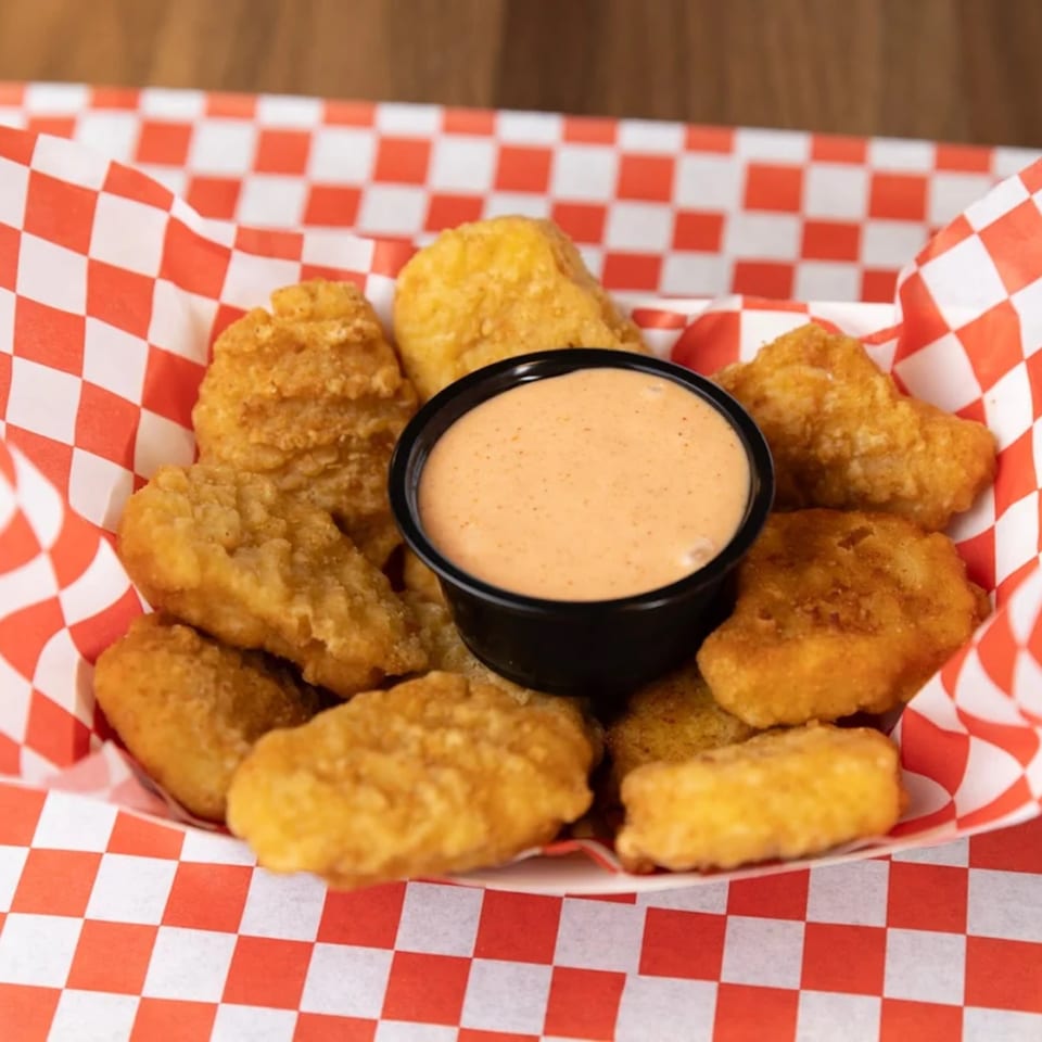 Golden-brown chicken nuggets with a side of dipping sauce in a red and white checkered basket.