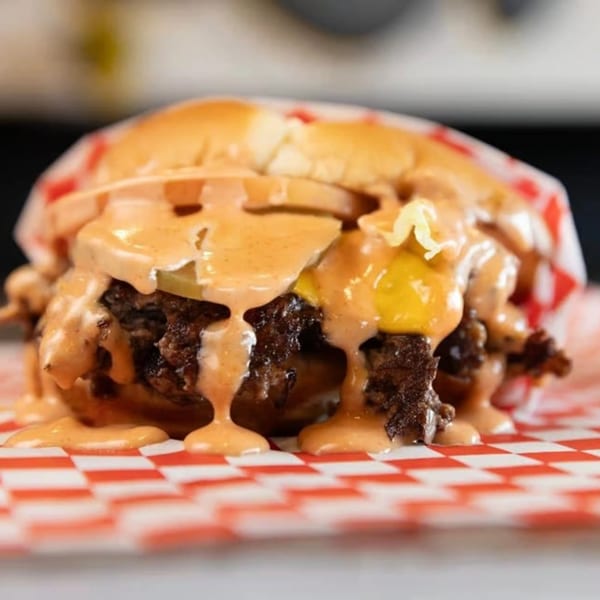 A SMA5H burger with melted cheese, pickles, and special sauce, served on red and white checkered paper.