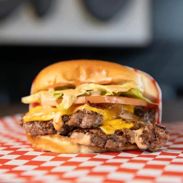 A SMA5H double cheeseburger with lettuce, tomato, and sauce on red and white checkered paper.